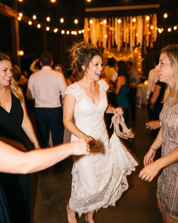 The bride, barefoot with her shoes in one hand, spins with two friends on the dance floor.